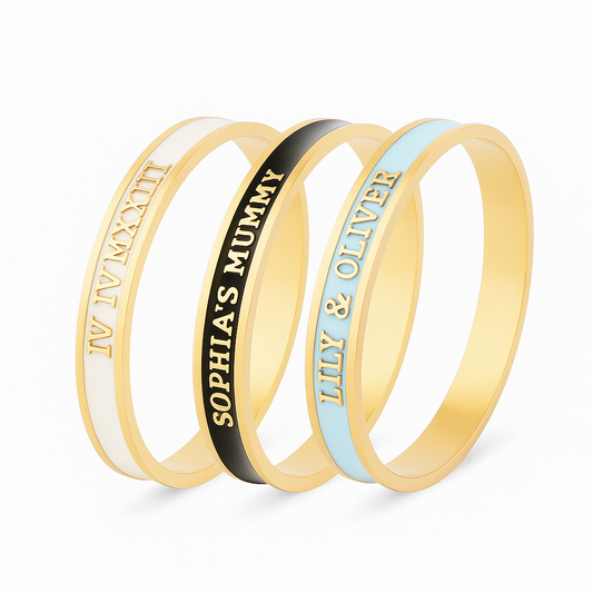 3 enamel bangles with different customised text on a white background. White and gold bangle reads 'IV IV MXXIII', black and gold bangle reads 'Sophia's Mummy', pale blue and gold bangle reads 'Lily & Oliver'